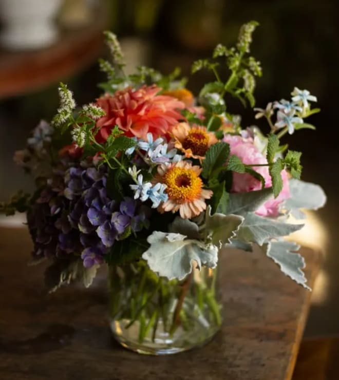 Mixed bouquet in a clear glass vase with pink, orange, purple, and blue flowers