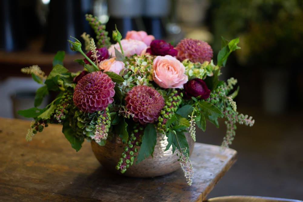 Low floral arrangement with pink and burgundy blooms in a metal bowl