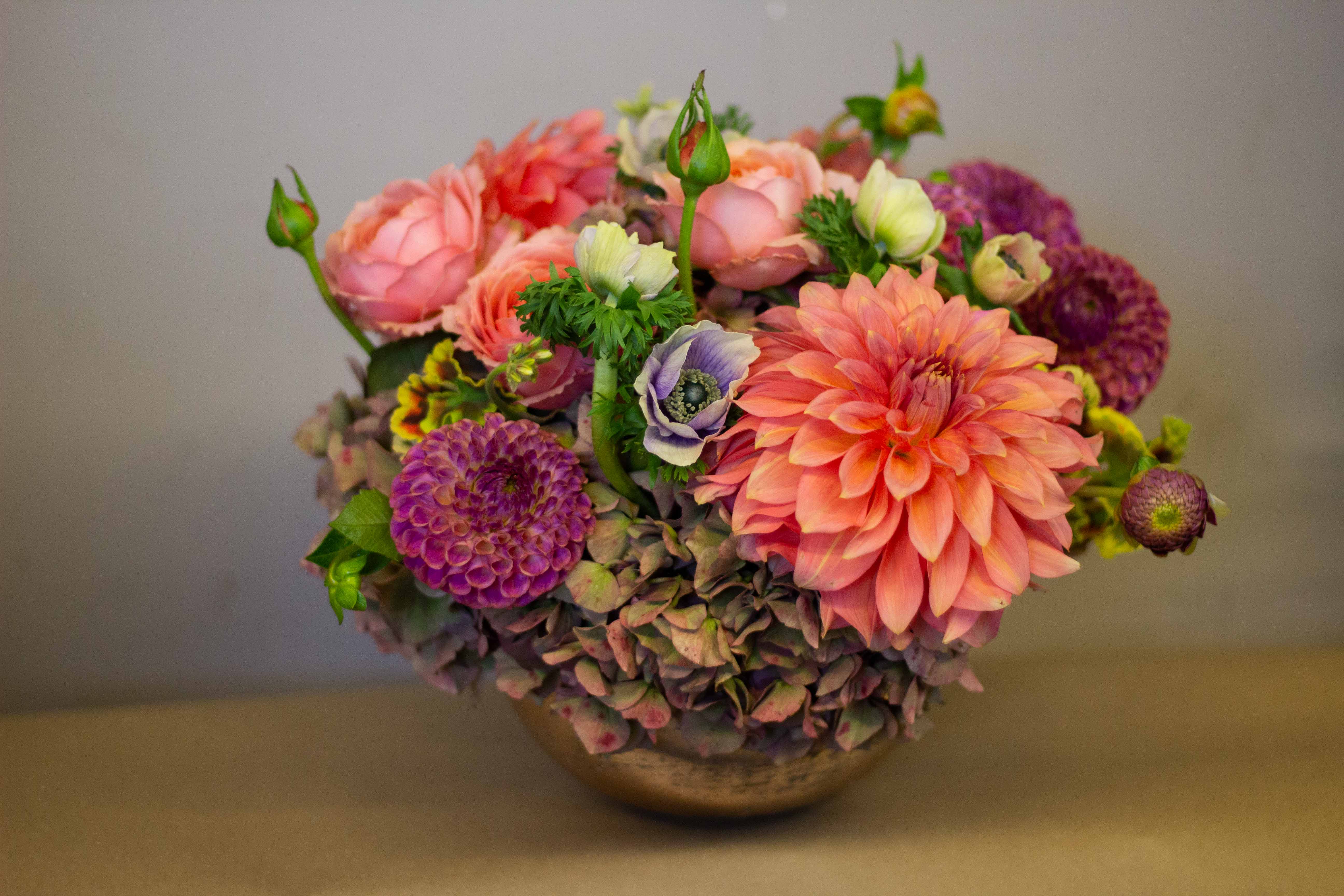 Mixed bouquet of pink, peach, and purple flowers in a low bowl vase