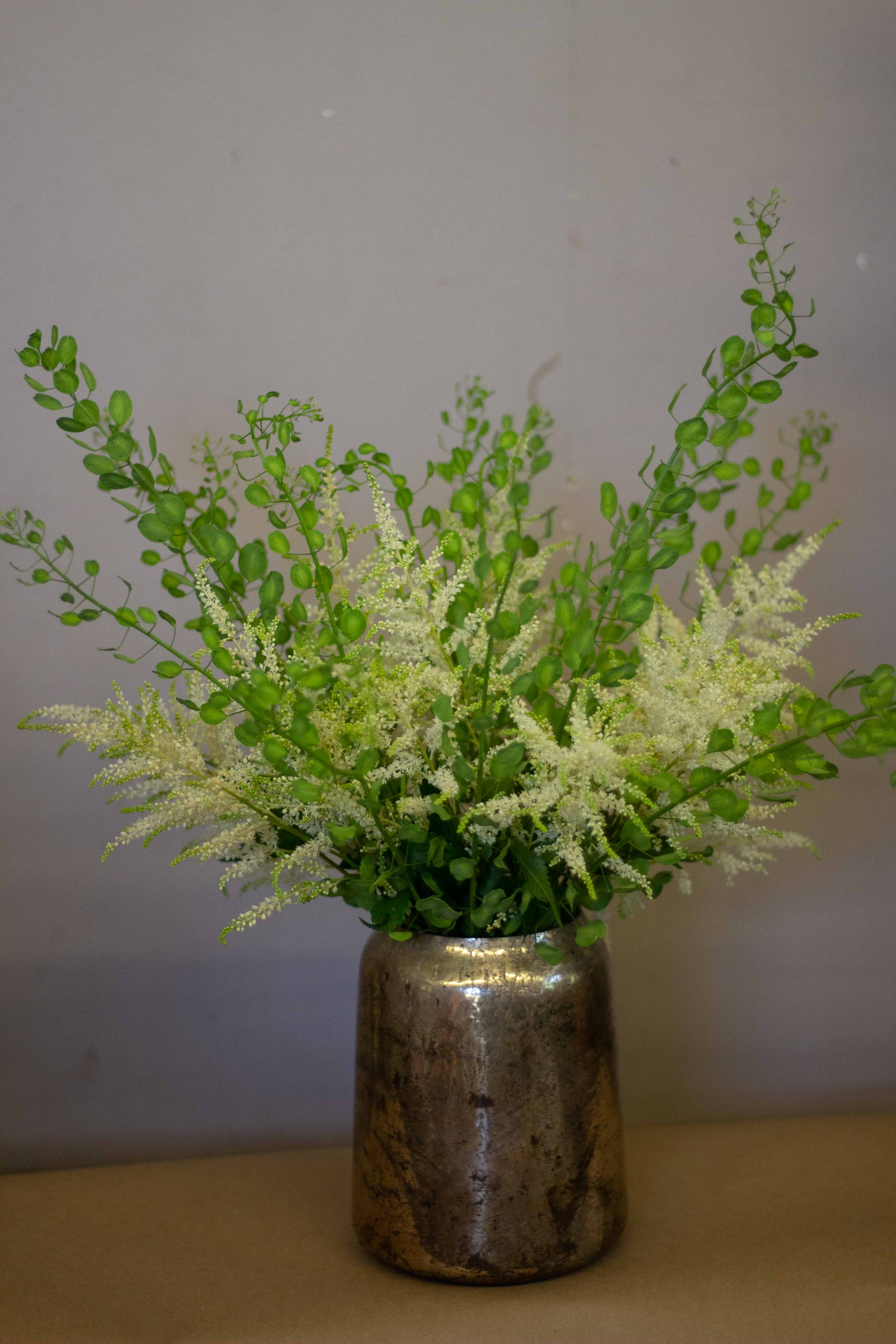 White filler flowers and green stems in a metallic vase