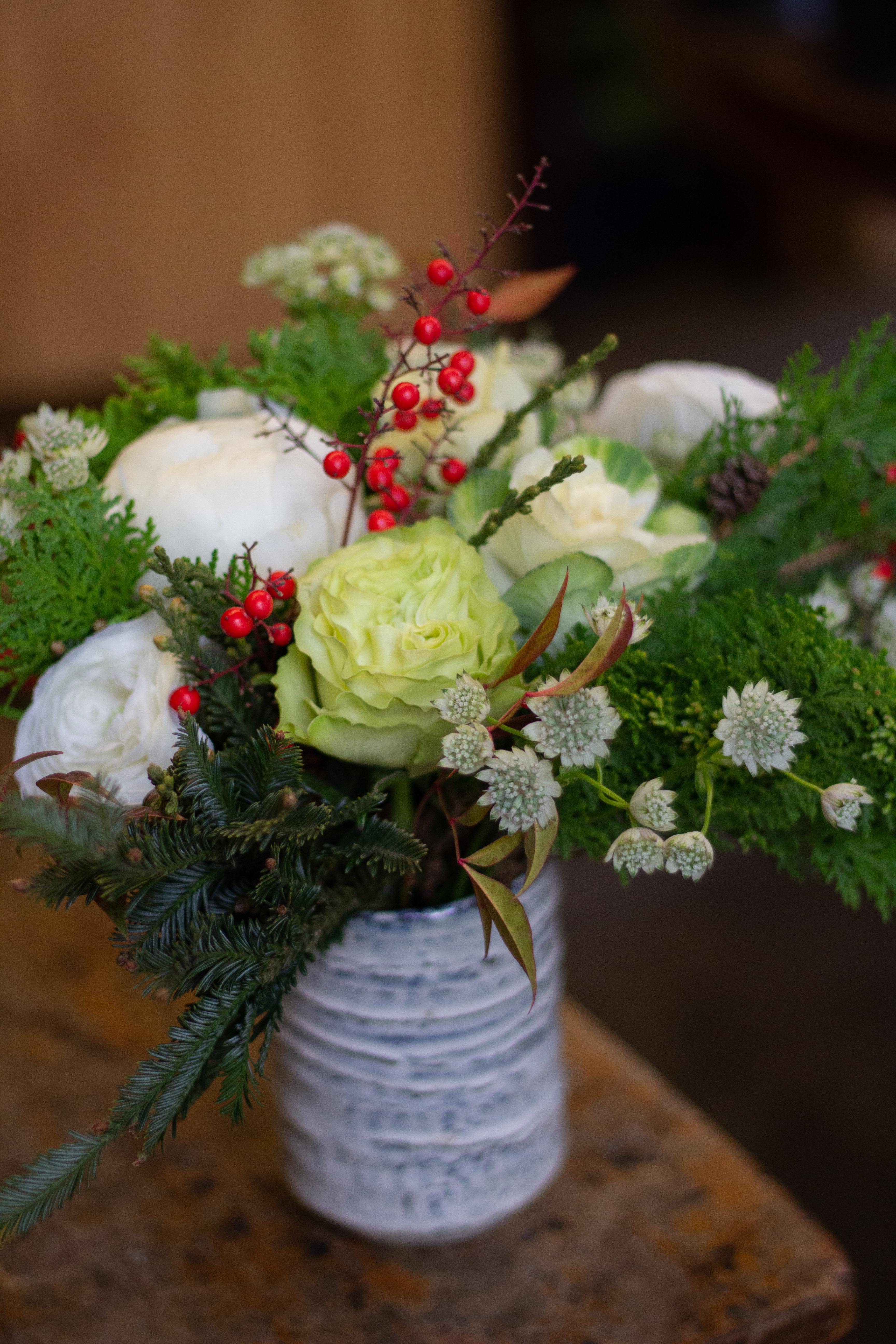 White and pale green floral arrangement in a white vase with red berry accents