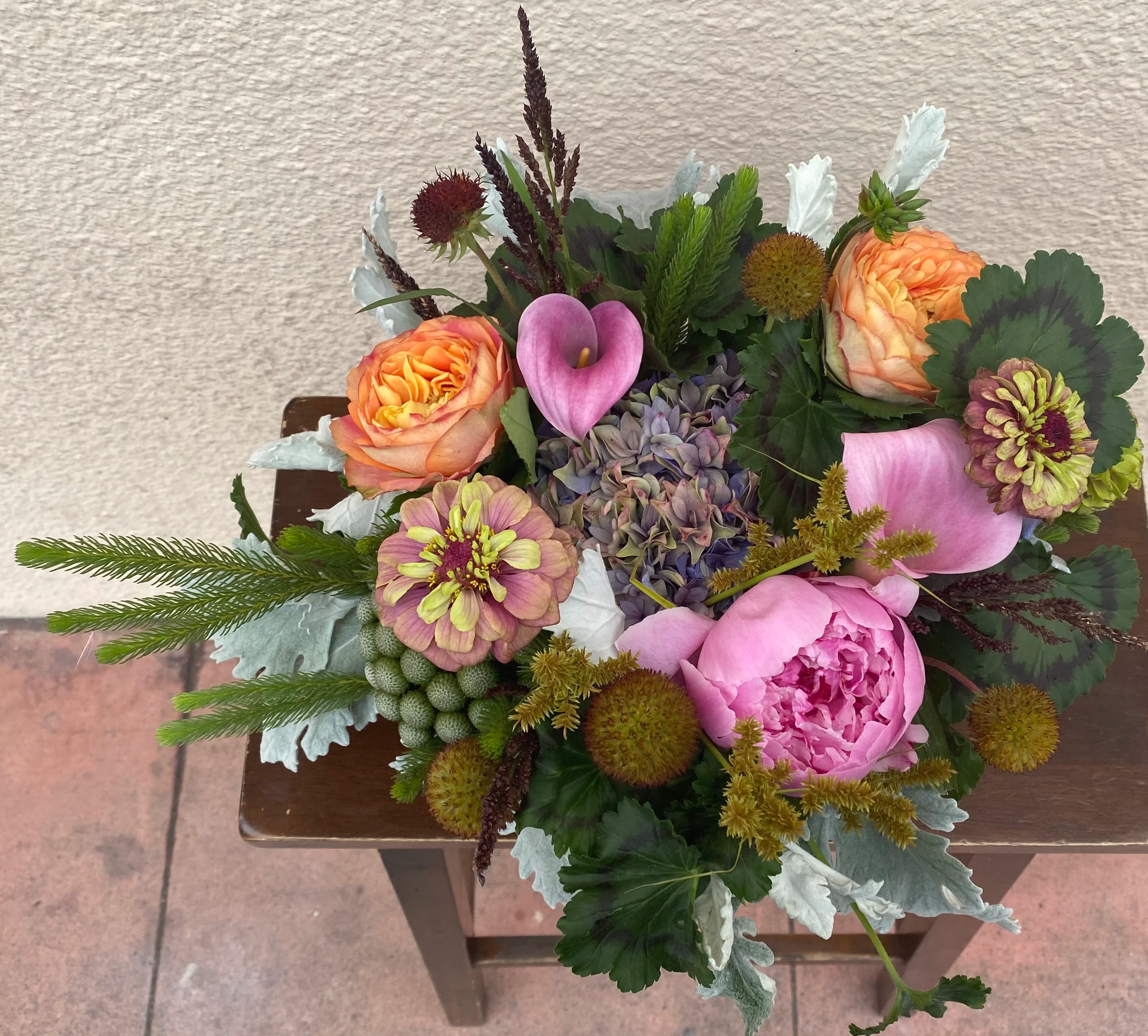 Mixed bouquet with pink peonies, orange roses, calla lilies, and zinnias