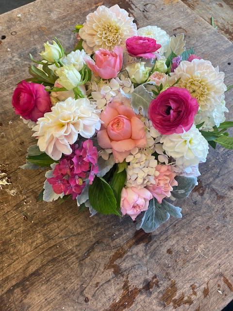 Round bouquet of pink, white, and peach flowers on a wooden surface