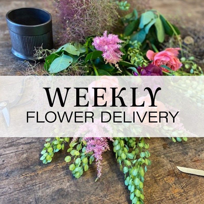 Loose floral arrangement with pink blooms and greenery beside a black container