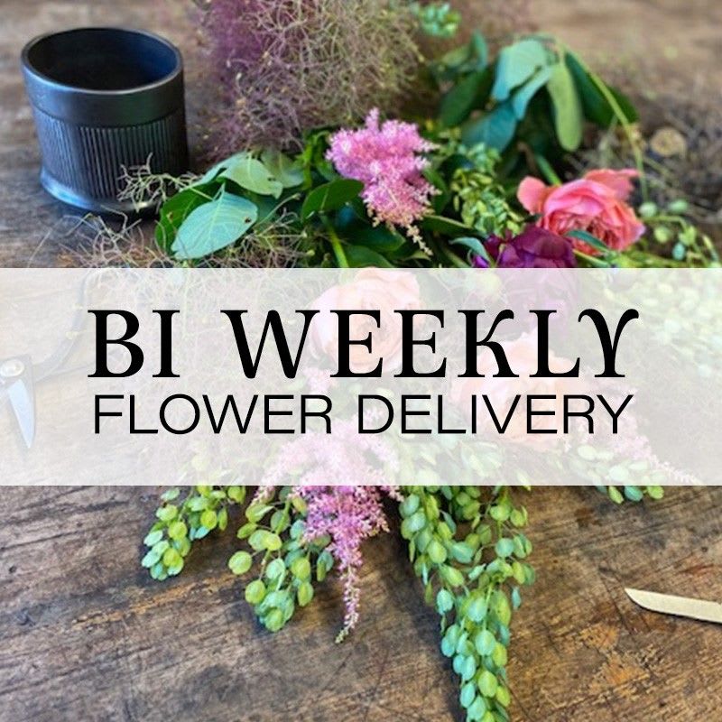 Loose floral arrangement with pink blooms and greenery beside a black cup
