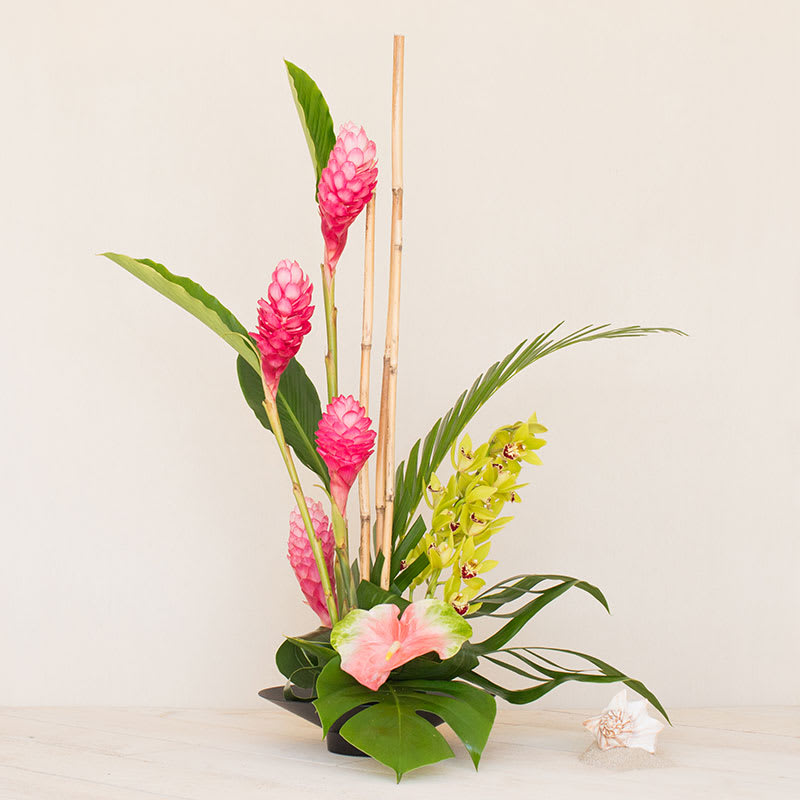 Tall tropical arrangement with pink flowers, green orchids, and bamboo in a black dish