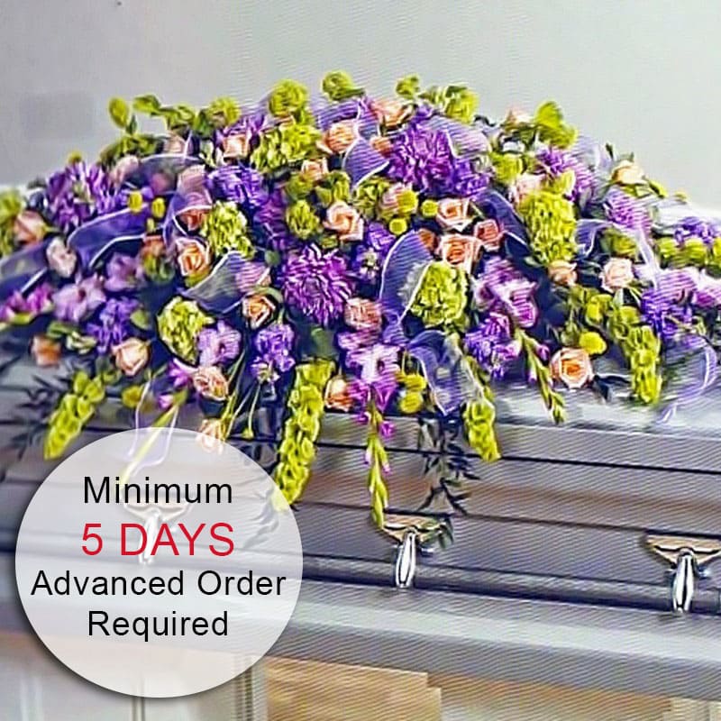 Large purple, green, and peach flower casket spray draped over a silver casket