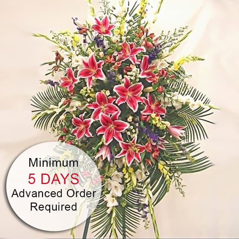 Tall standing spray with pink lilies and mixed white and yellow flowers on a metal easel