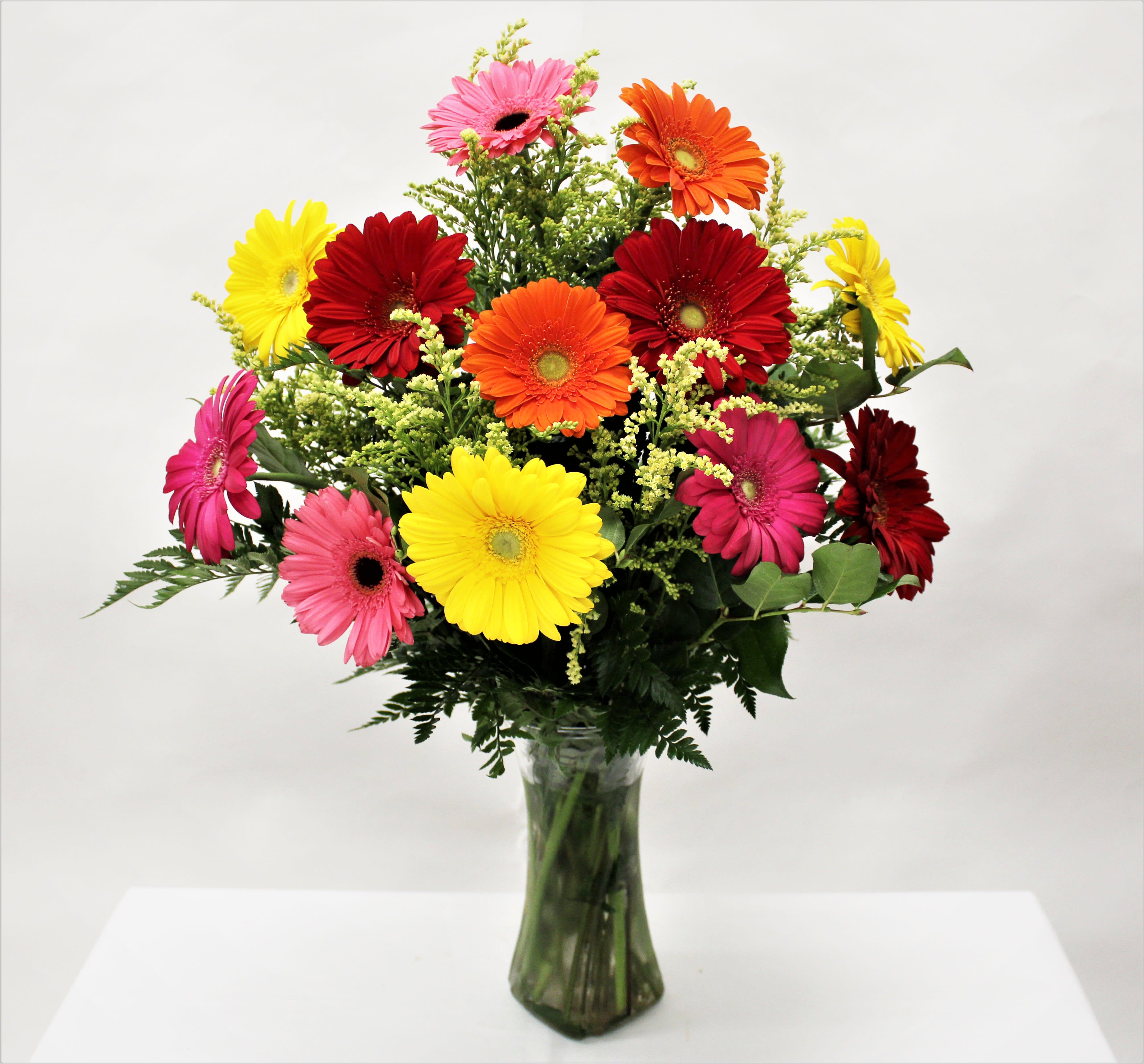 Vase arrangement of bright mixed-color gerbera daisies with small yellow filler blooms.