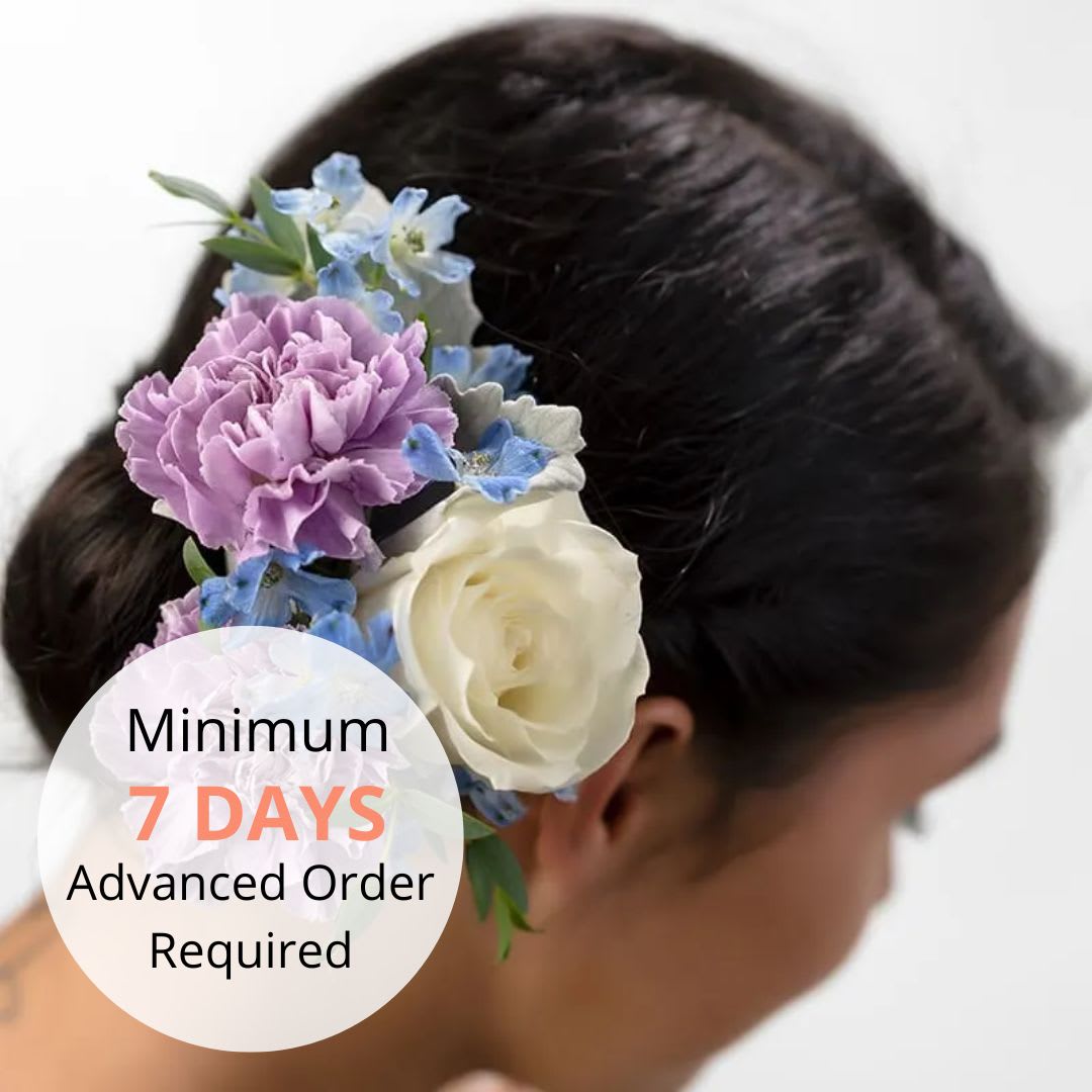 Floral hairpiece with purple carnation, white rose, and blue blooms worn in dark hair.