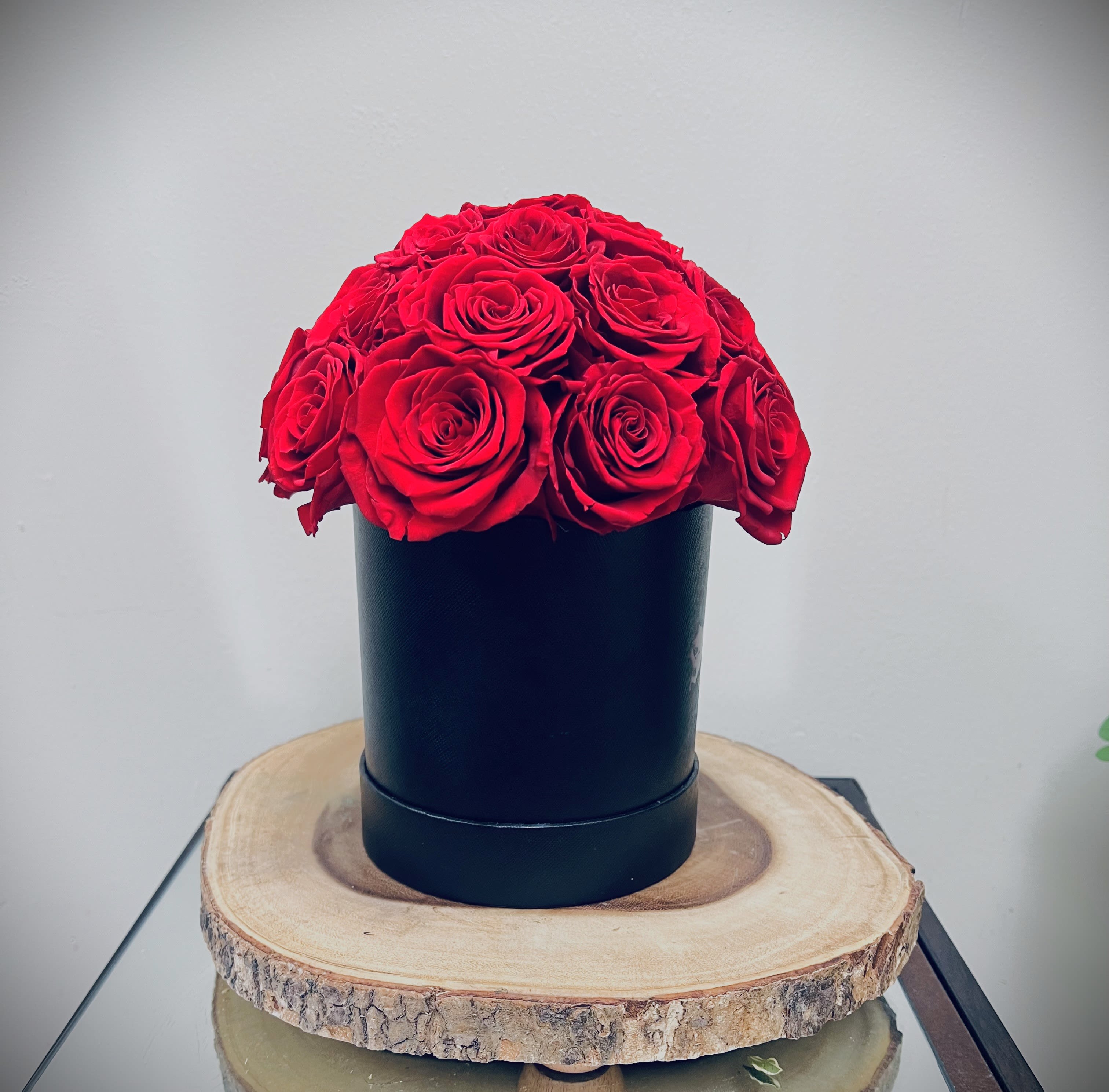 Dome of red roses arranged in a black cylinder box on a wood slice base