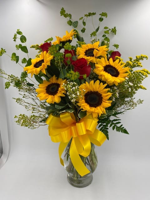 Bouquet of sunflowers and red roses in a glass vase with a yellow ribbon