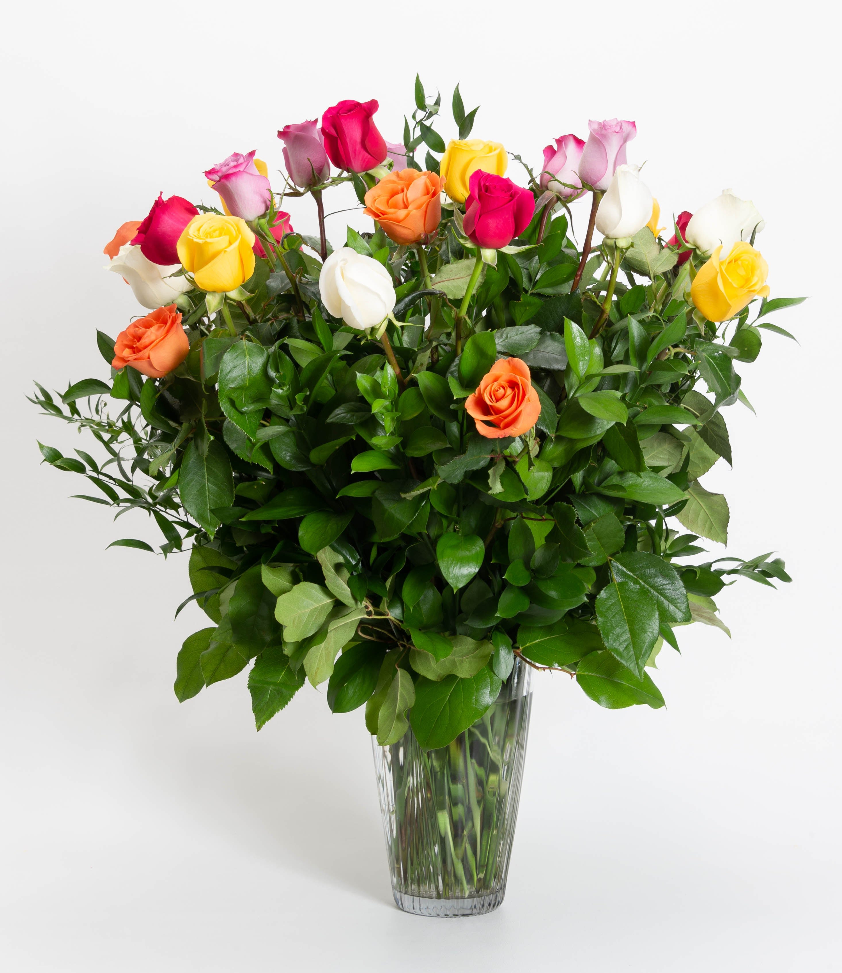 Mixed roses in a clear glass vase with dense greenery