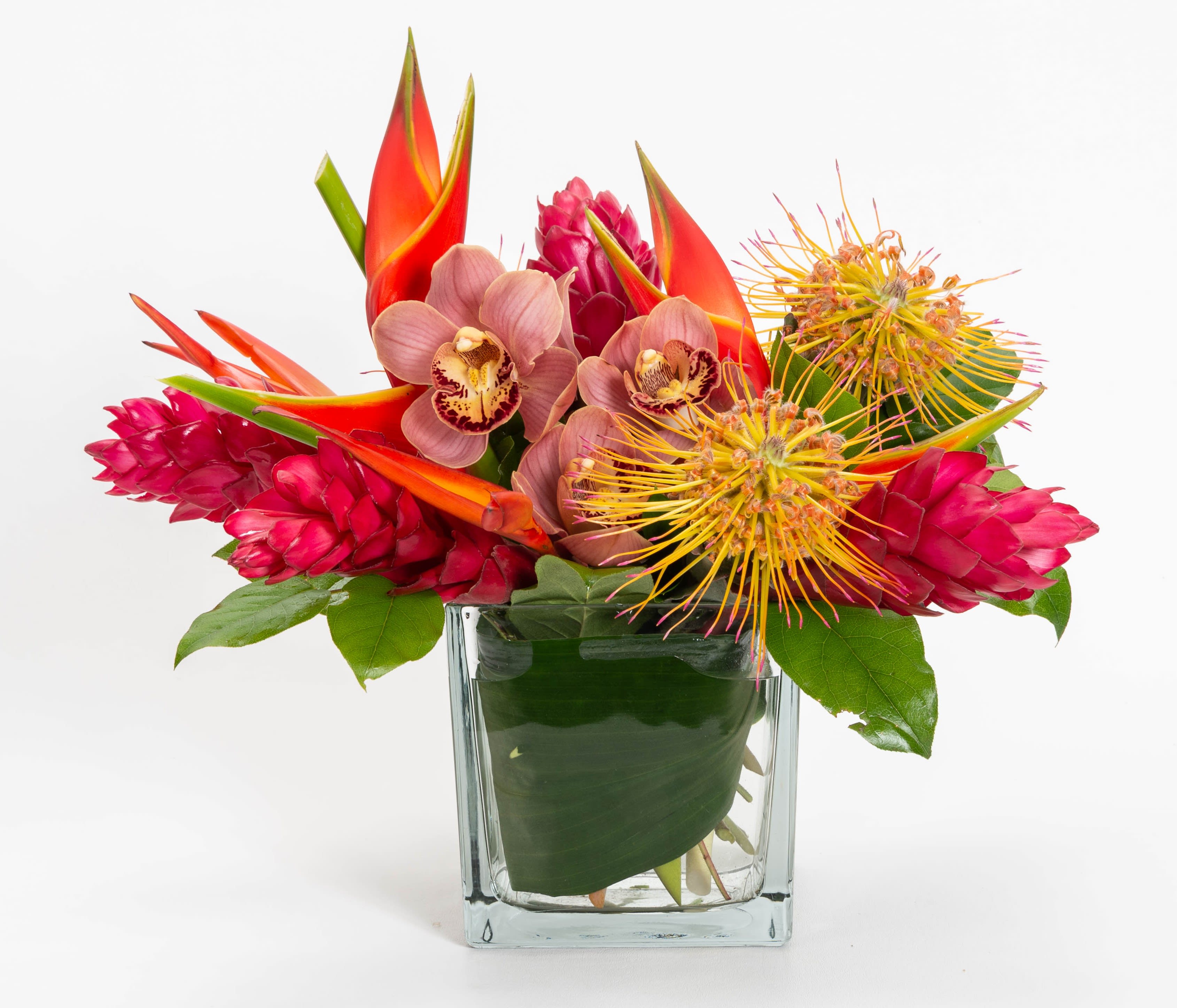 Tropical bouquet in a clear glass vase with pink orchids and red-orange blooms