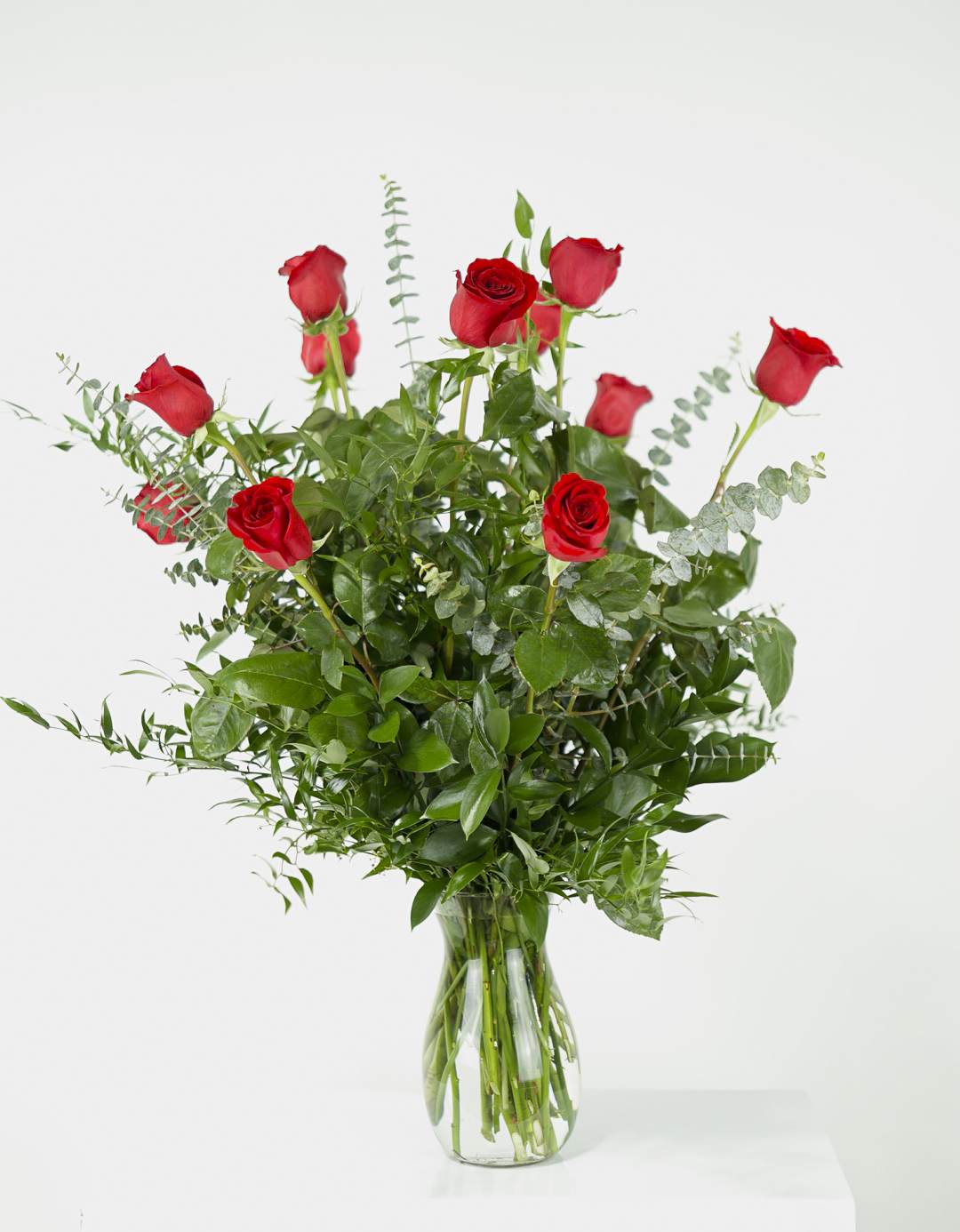 Red roses arranged in a clear glass vase with mixed greenery