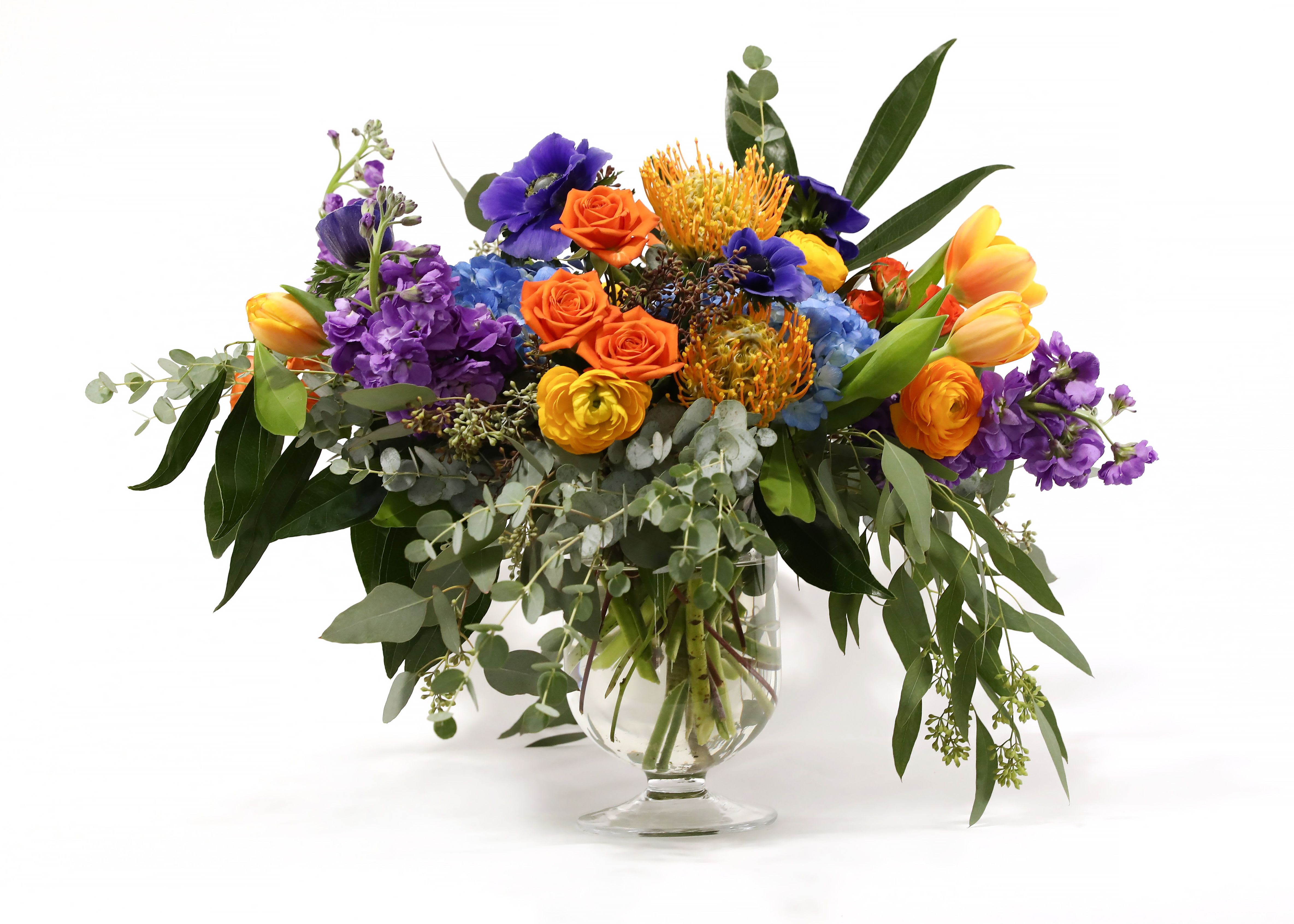 GARDEN VIEW  - THIS STUNNING GLASS PEDESTAL ARRANGEMENT HAS ALL YOUR FAVORITES. HYDRANGEAS, SPRAY ROSES, PIN CUSHIONS, STOCK, ANEMONES, RANUNCULUS, TULIPS, AND EUCALYPTUS.