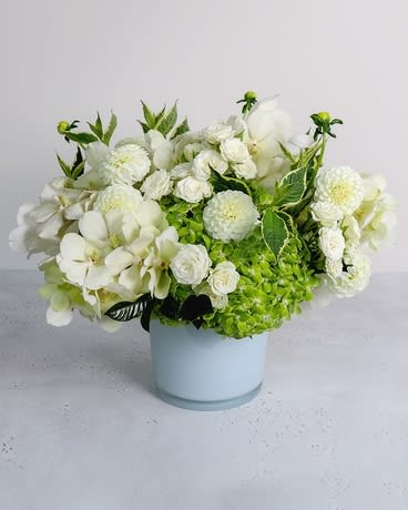 White floral arrangement in a pale blue vase with green accents