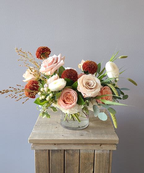 Pink and white roses in a clear glass vase with orange pom-pom flowers