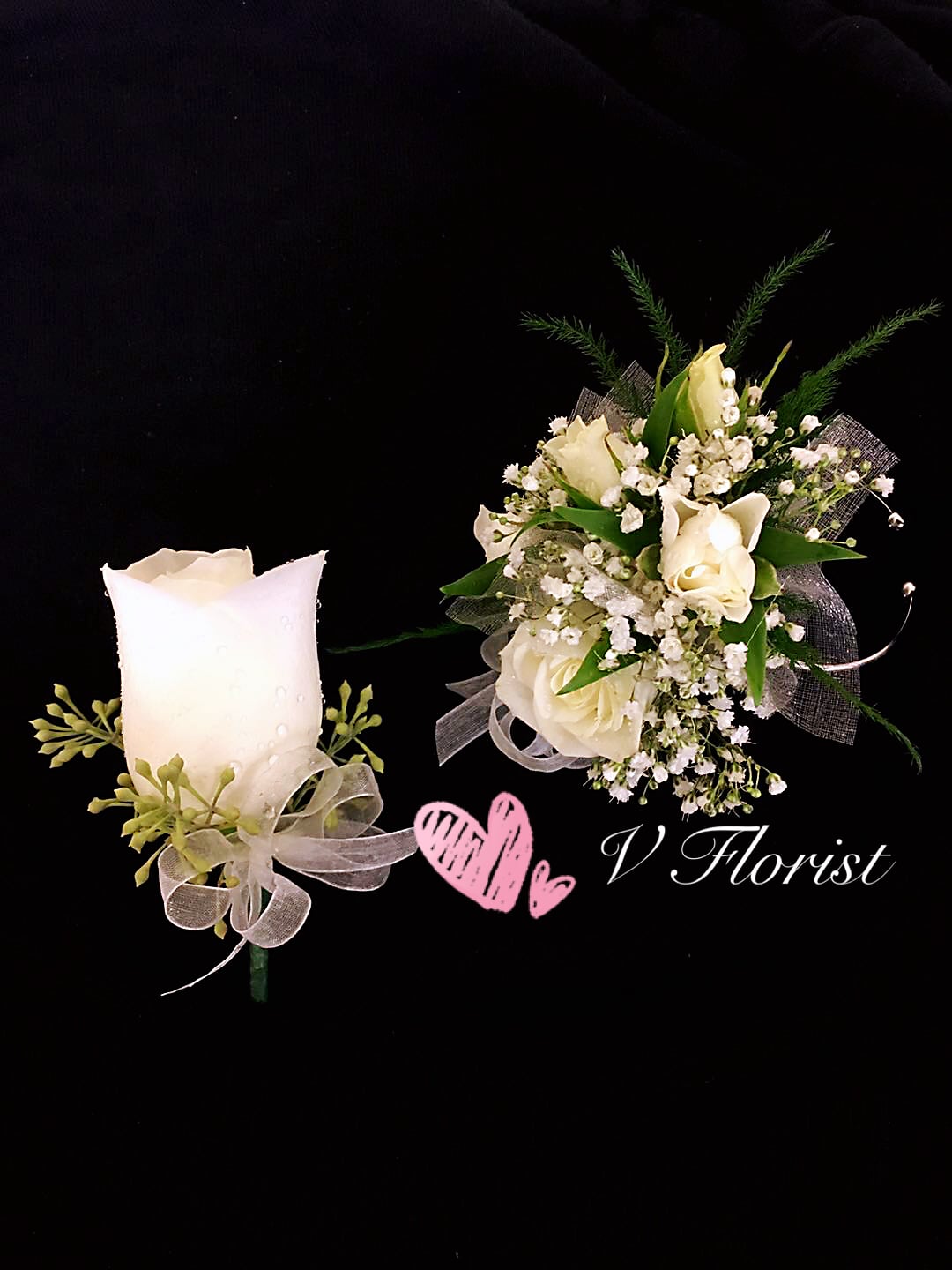 White rose boutonniere and matching wrist corsage with white ribbons on a black background.