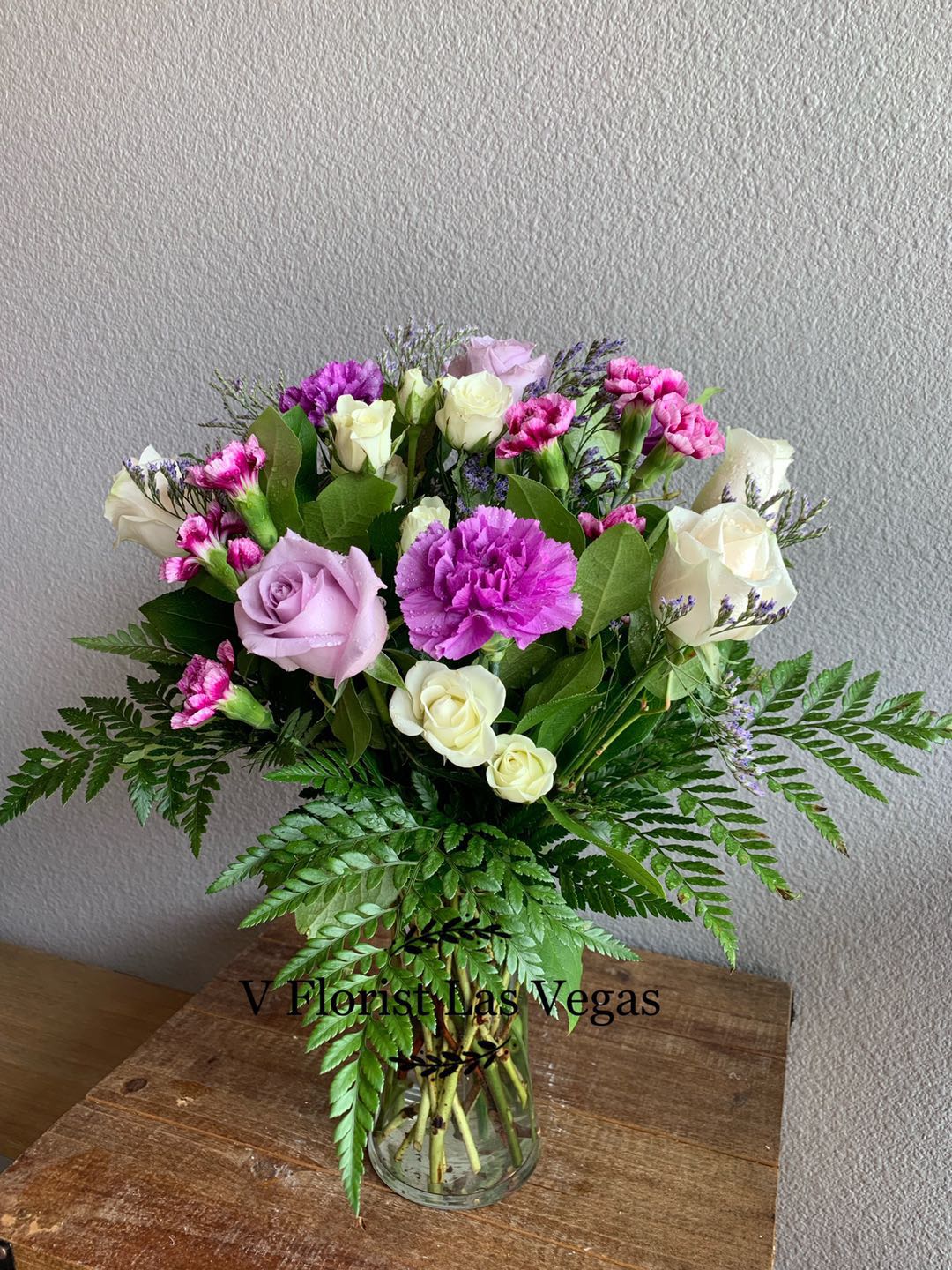 Mixed bouquet of lavender roses, white roses, and purple carnations in a clear glass vase