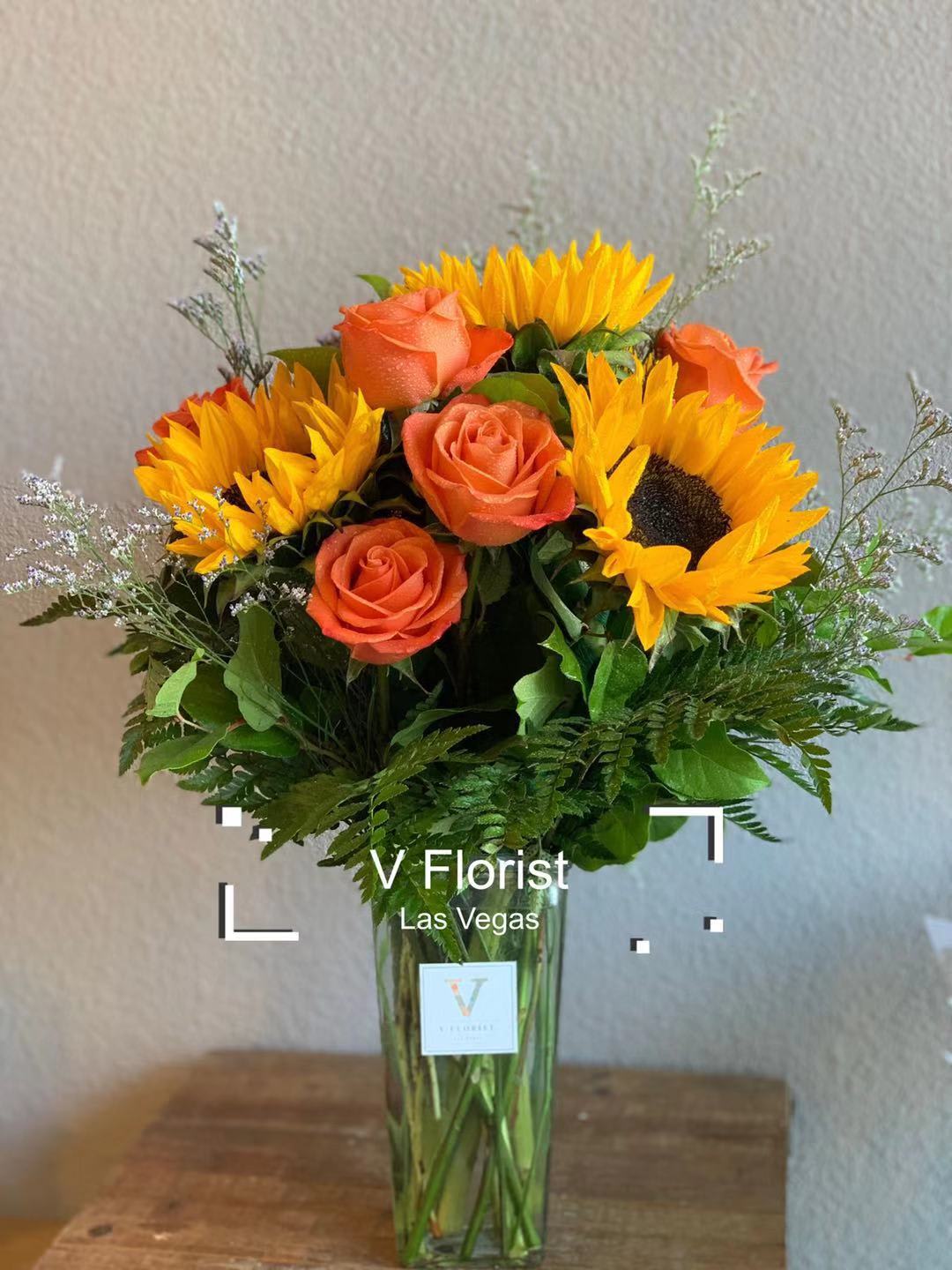 Tall vase of yellow sunflowers and orange roses in a clear glass rectangular vase.