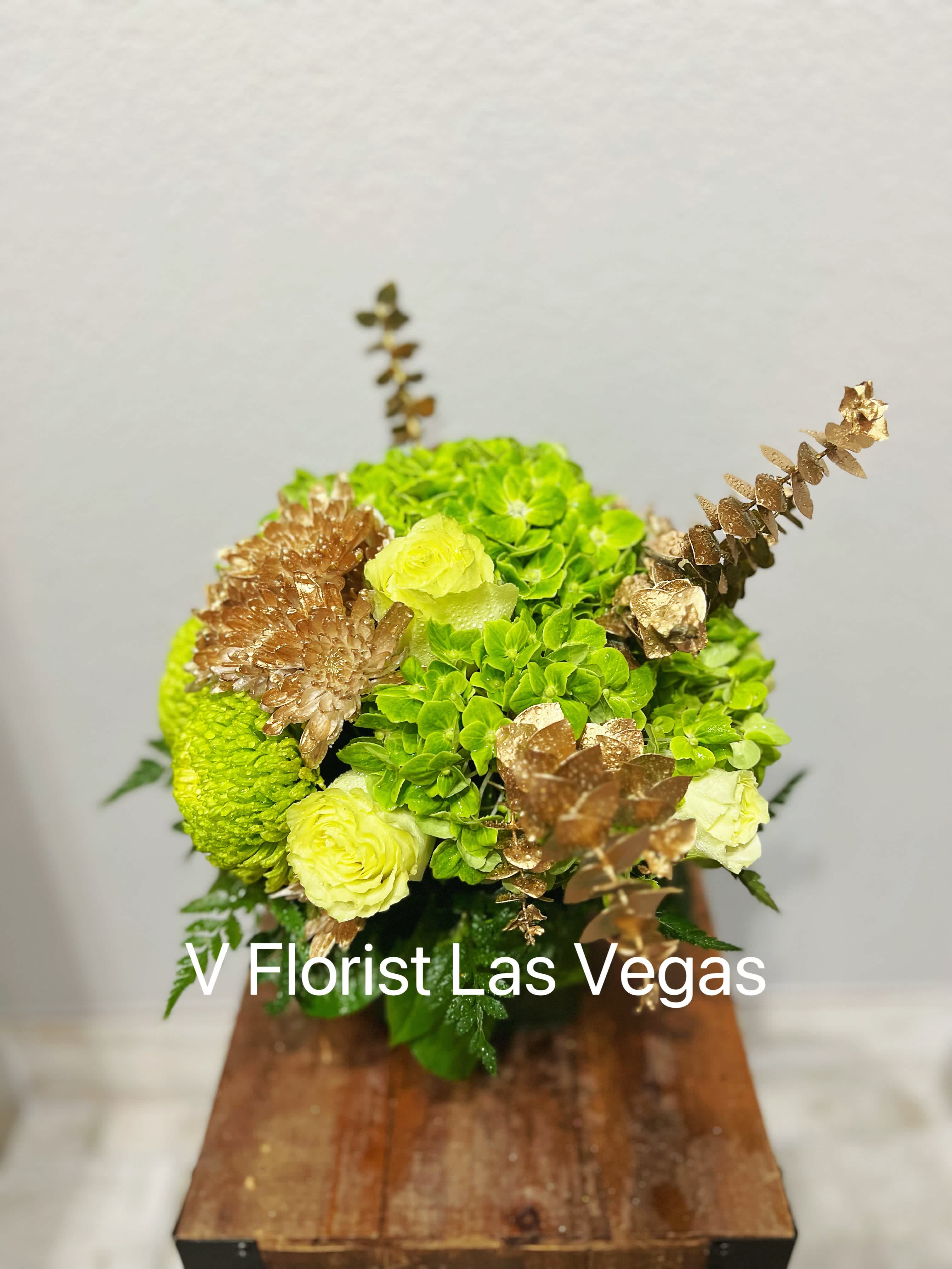 Green and pale yellow floral arrangement with gold accents in a wooden container