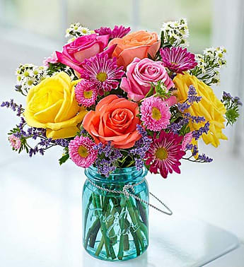 Colorful bouquet of roses and daisies in a blue glass jar