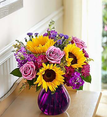 Bouquet of sunflowers and pink roses in a purple glass vase