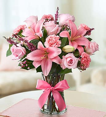 Pink lilies and roses arranged in a glass vase with a pink ribbon