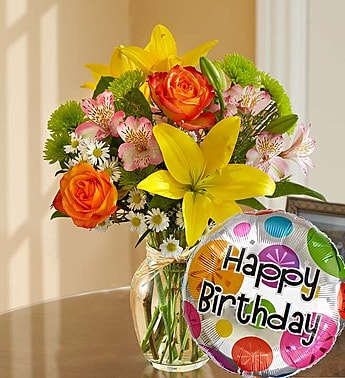 Bouquet of yellow lilies and orange roses in a glass vase with a birthday balloon