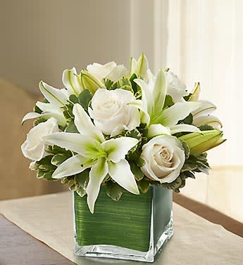 White lilies and roses arranged in a square glass vase