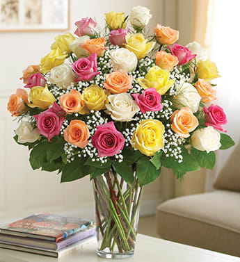 Mixed bouquet of roses in pink, yellow, peach, and white in a glass vase