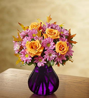 Orange roses and pink daisies in a purple glass vase
