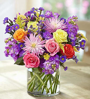 Mixed bouquet of roses and purple flowers in a clear glass vase