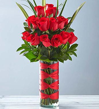 Tall bouquet of red roses in a clear glass vase with red ribbon bows