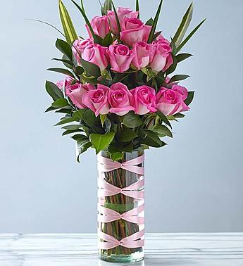 Pink roses arranged in a tall glass vase with pink ribbon