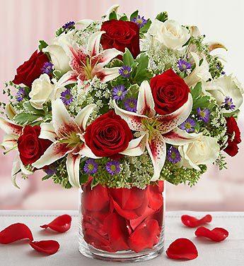 Bouquet of red roses and white lilies in a glass vase with rose petals