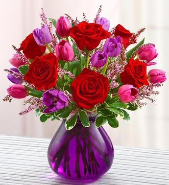 Bouquet of red roses and pink-purple tulips in a purple glass vase