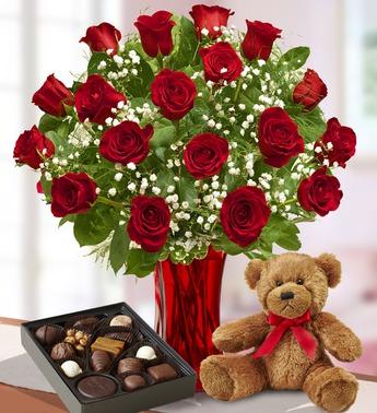 Red roses in a vase with a teddy bear and box of chocolates