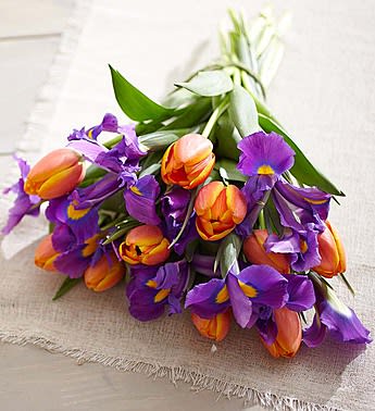Bouquet of orange tulips and purple irises on a light fabric surface