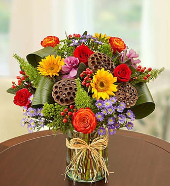 Mixed bouquet of roses, sunflowers, and purple daisies in a glass vase
