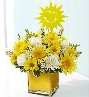 Yellow and white flower arrangement in a square glass vase with a smiling sun topper