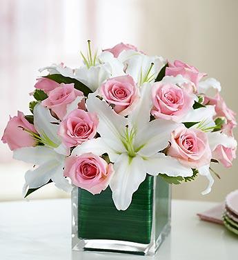 Pink roses and white lilies arranged in a clear square vase