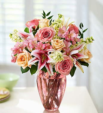 Pink and peach roses with lilies in a pink glass vase