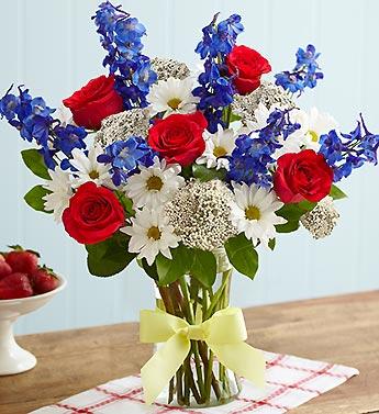 Bouquet of red roses, white daisies, and blue flowers in a glass vase