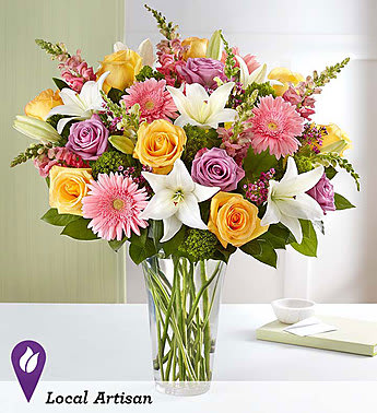 Mixed bouquet of roses, lilies, and pink daisies in a clear glass vase