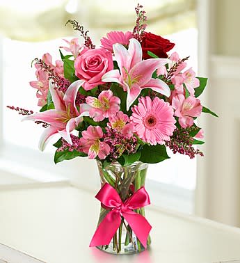 Pink and white mixed bouquet in a clear glass vase with a pink ribbon