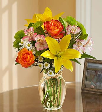 Bouquet of yellow lilies, orange roses, and pink alstroemeria in a glass vase
