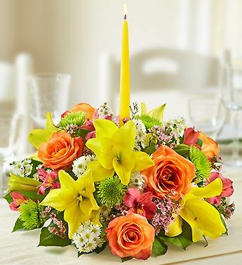 Low floral centerpiece with yellow lilies, orange roses, and a tall yellow candle