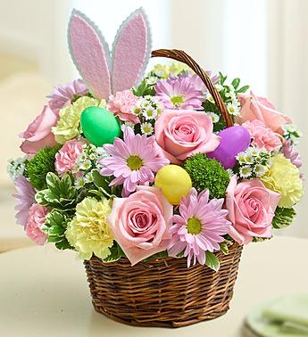 Basket of pink roses and daisies with pastel Easter eggs and bunny ears